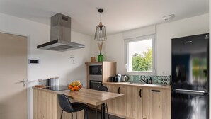 Une cuisine moderne dotée d’un îlot central, d’un réfrigérateur noir et d’une fenêtre offrant une vue sur la verdure.