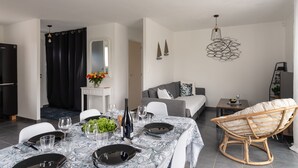 Un espace repas moderne avec une table dressée pour quatre personnes, un canapé, un fauteuil en osier et une petite table d’appoint agrémentée d’une plante.