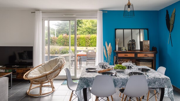 Un coin repas avec une table dressée pour quatre personnes, une chaise en osier et un téléviseur en arrière-plan.
