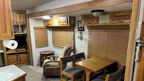 Une cuisine compacte avec des meubles de rangement en bois, une table à manger avec des chaises, une petite table ronde et un luminaire fixé au mur.
