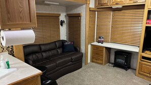 Un espace de vie compact comprenant un canapé, des meubles en bois, une petite kitchenette et une poubelle.