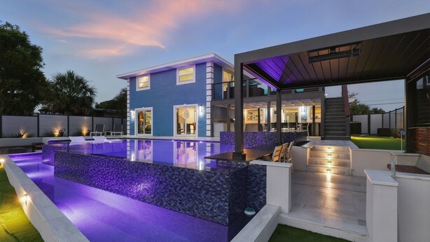 A modern house with a large outdoor pool, a covered patio, and a well-lit interior.