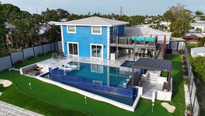 A modern house with a large swimming pool, a covered patio, and a well-maintained lawn.