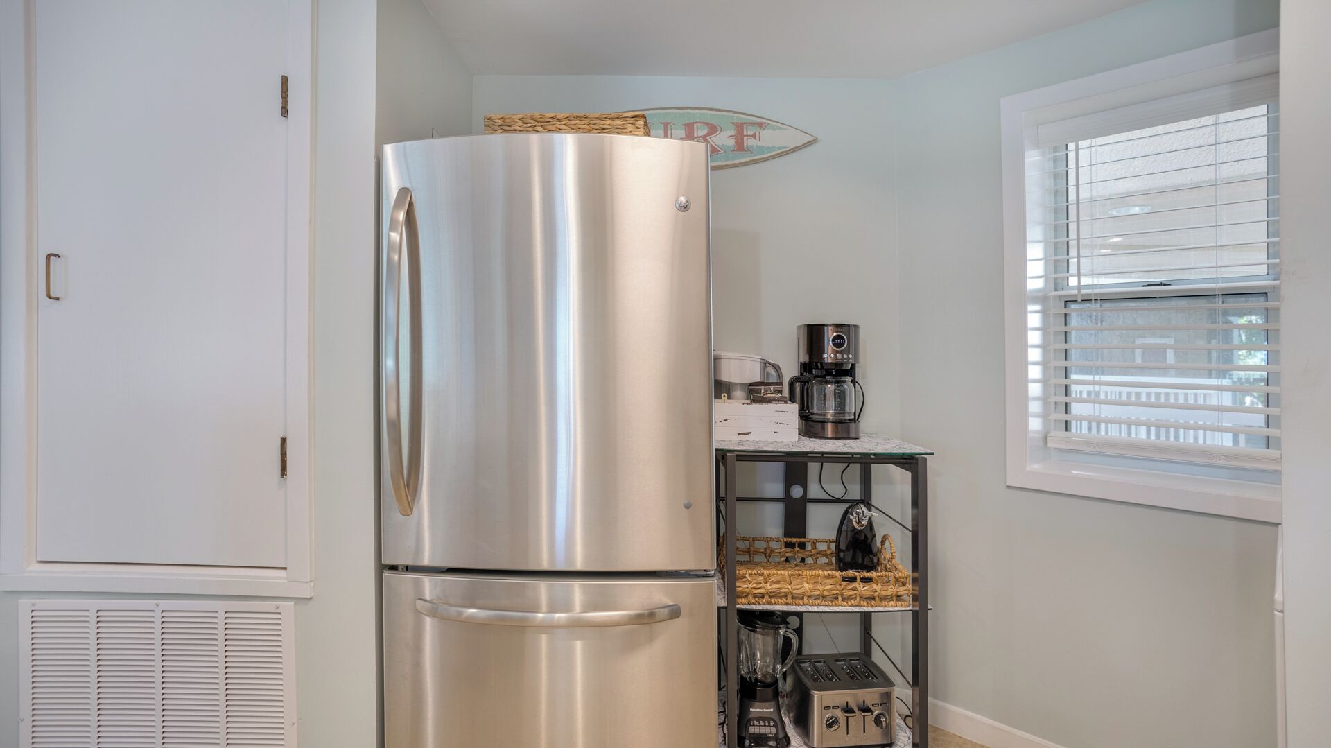 A compact kitchen with a stainless steel refrigerator, a coffee maker, and a toaster on a glass shelf.
