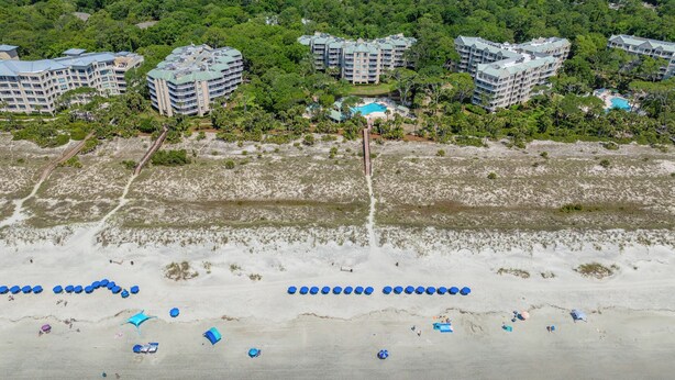 Una vista aerea di un resort costiero con diversi edifici a grattacielo, una spiaggia sabbiosa con ombrelloni e una limpida vista dell'oceano.