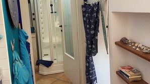 A bathroom with a glass shower door, a towel rack with towels, and a shelf with books and decorative items.