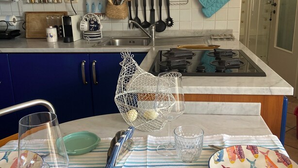 A kitchen with a striped tablecloth, a sink, and various kitchen utensils.