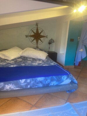 A bedroom with a bed, a wall-mounted compass, a nightstand, and a tiled floor.