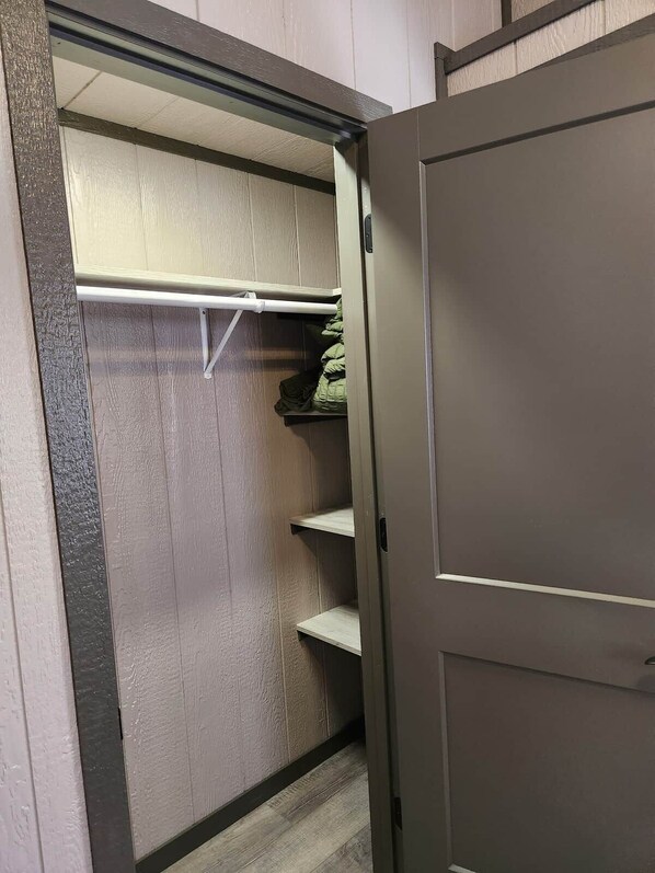 A closet with shelves and hanging space, a door, and a partial view of a wooden floor.