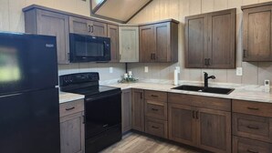 A kitchen with wooden cabinets, a black refrigerator, a microwave, a stove, and a sink.