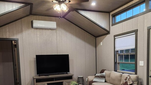 A modern living room with a flat-screen TV, a sofa, a coffee table, and a ceiling fan.