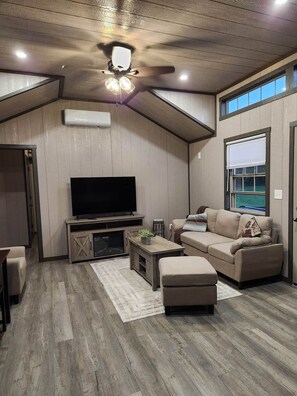 A modern living room with a flat-screen TV, a sofa, a coffee table, and a ceiling fan.