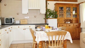 A kitchen with white cabinets, a microwave, a toaster, and a table set for dining. - The Dairy at Copper Beeches (Petersfield)