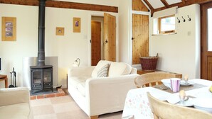 A cozy living room with a fireplace, a sofa, a dining table with chairs, and wooden beams on the ceiling. - The Dairy at Copper Beeches (Petersfield)