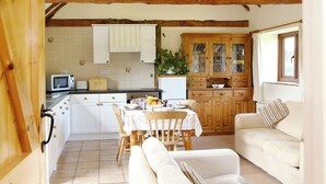 A cozy kitchen with wooden beams, a dining table, and a sofa in a bright room. - The Dairy at Copper Beeches (Petersfield)