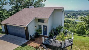 A single-story house with a garage, a front porch with seating, and a small deck. - Views of Osage Golf Course & Osage River, 3 Balconies, Game Room, Sleeps 9 (Kaiser)