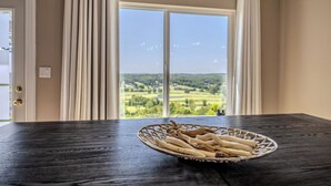 A dining table with a basket of baguettes in front of a large window with a view of a green landscape. - Views of Osage Golf Course & Osage River, 3 Balconies, Game Room, Sleeps 9 (Kaiser)