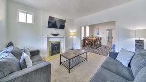 Una sala de estar con chimenea, un televisor montado encima y una zona de comedor con una mesa y sillas.