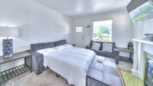 Un dormitorio con una cama, un sofá gris, una mesita, una lámpara y un televisor.
