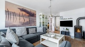 A modern living room with a grey sofa, a glass coffee table, a large painting of a sunset, a TV, and a fireplace.