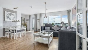 A modern living room with a dining area, large windows, and a view of the sea.