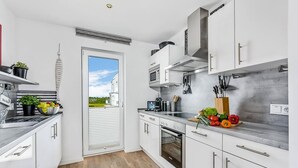A modern kitchen with white cabinets, stainless steel appliances, and a view through the door.