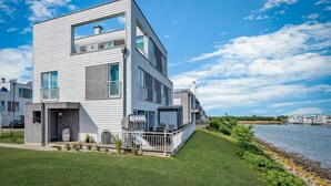 A modern two-story house with a balcony, a small porch, and a view of a lake.