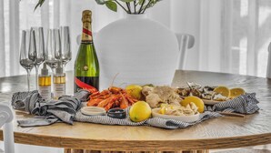 A round wooden table with a bottle of champagne, seafood, and condiments. - High Noon - Pet Friendly Eden (Eden)