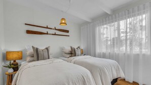 A bedroom with two beds, a hanging light fixture, and a window with sheer curtains. - High Noon - Pet Friendly Eden (Eden)