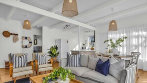 A modern living room with a sofa, armchairs, a coffee table with plants, and a dining area with a table and chairs. - High Noon - Pet Friendly Eden (Eden)