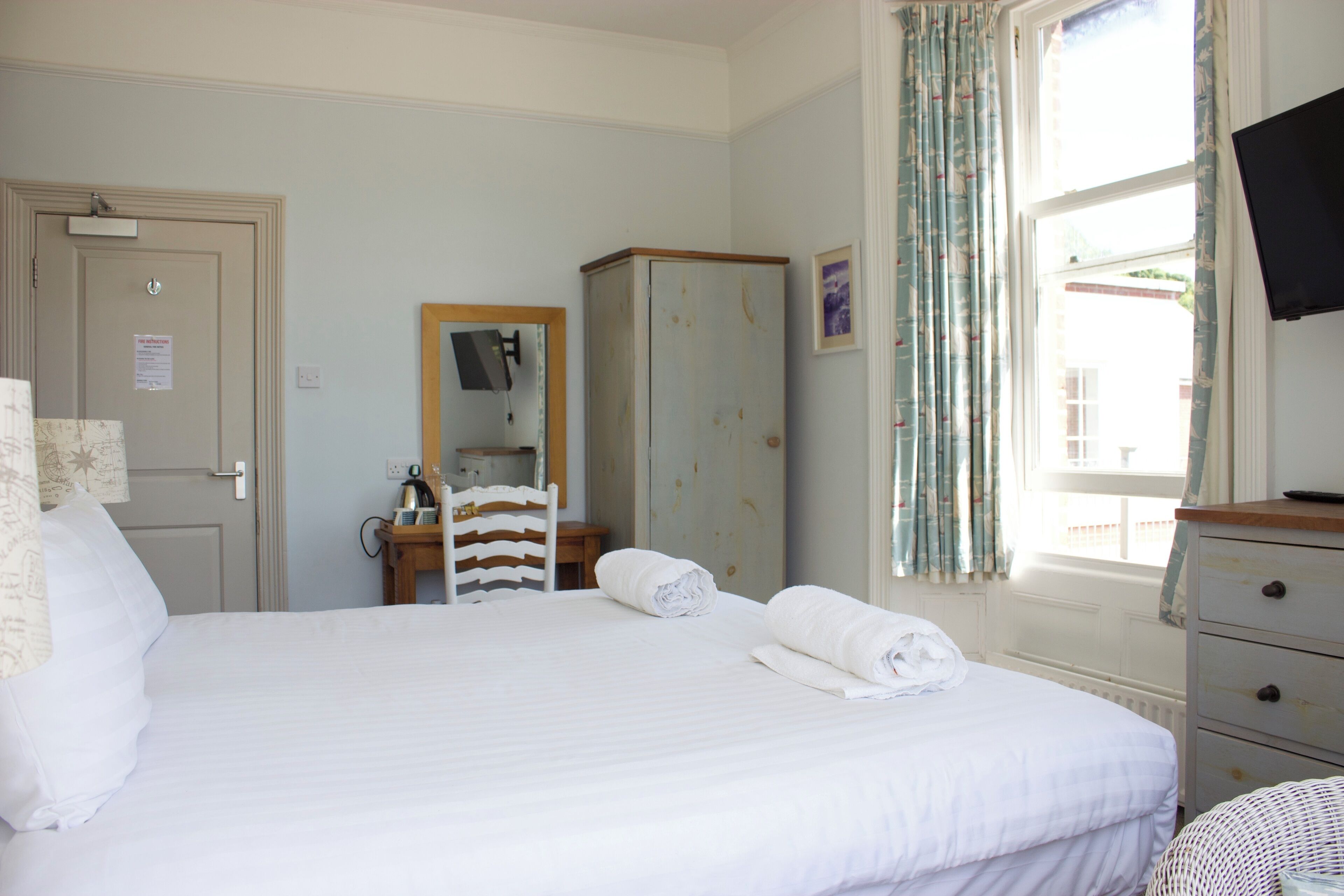 A hotel room with a bed, a wardrobe, a desk with a chair, a television, and a window with curtains.