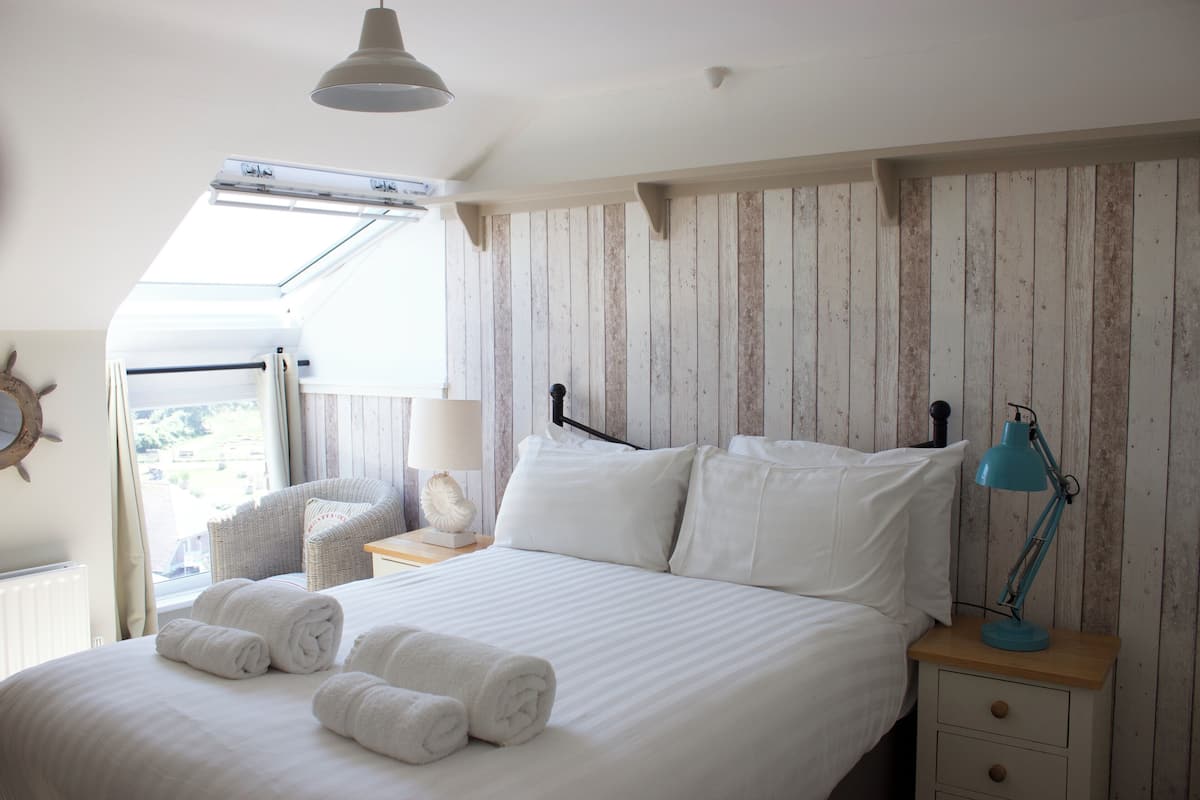 A bedroom with a bed, a nightstand, a lamp, and a view of the outside.
