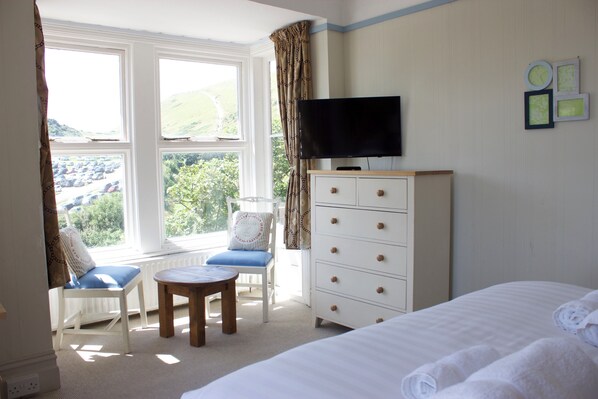 A bedroom with a bed, a TV, a dresser, a chair, and a small table.