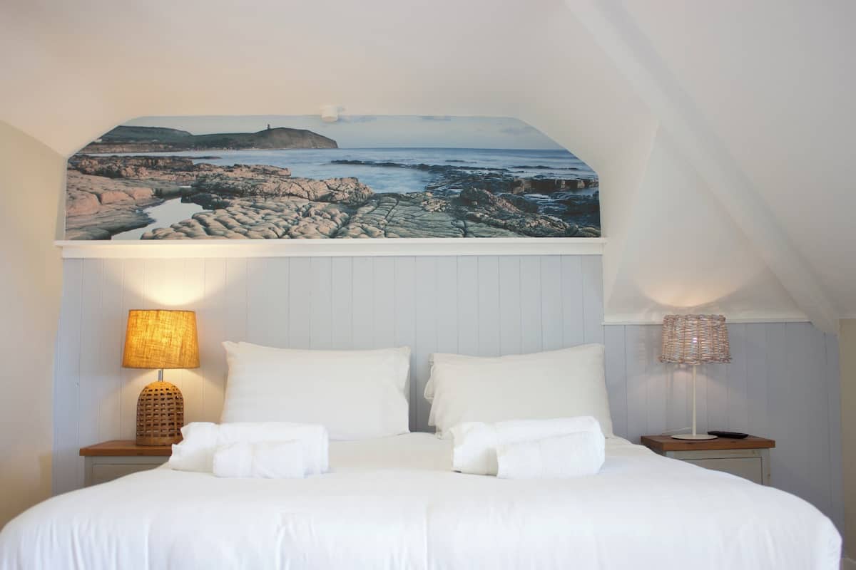 A bedroom with a bed, two bedside tables, a lamp on each table, and a large picture above the bed.