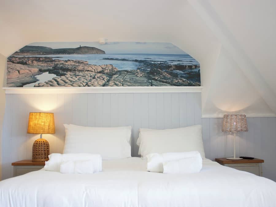 A bedroom with a bed, two bedside tables, a lamp on each table, and a large picture above the bed.
