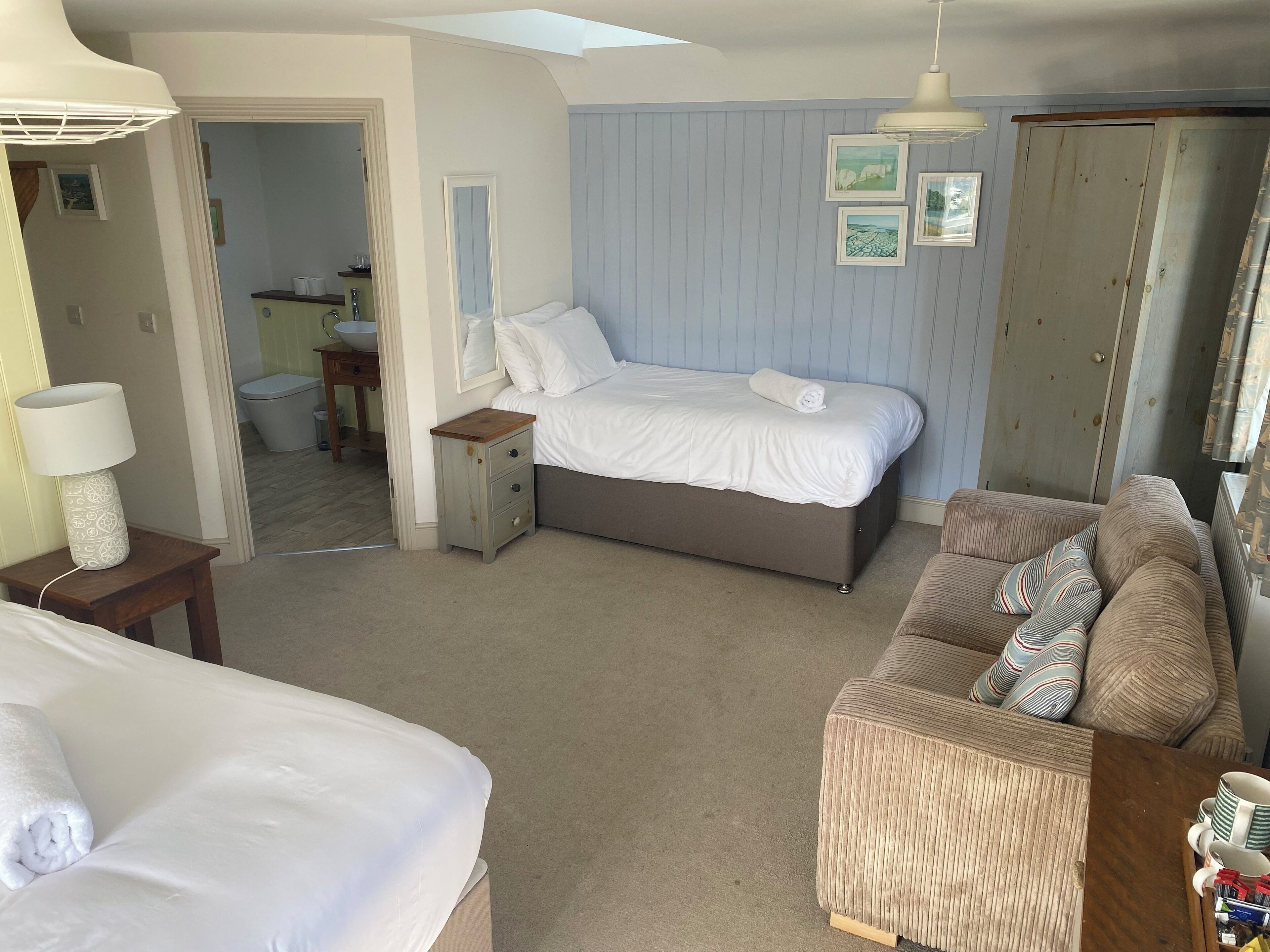 A bedroom with a bed, a bedside table with a lamp, a dresser, a sofa, and a door.