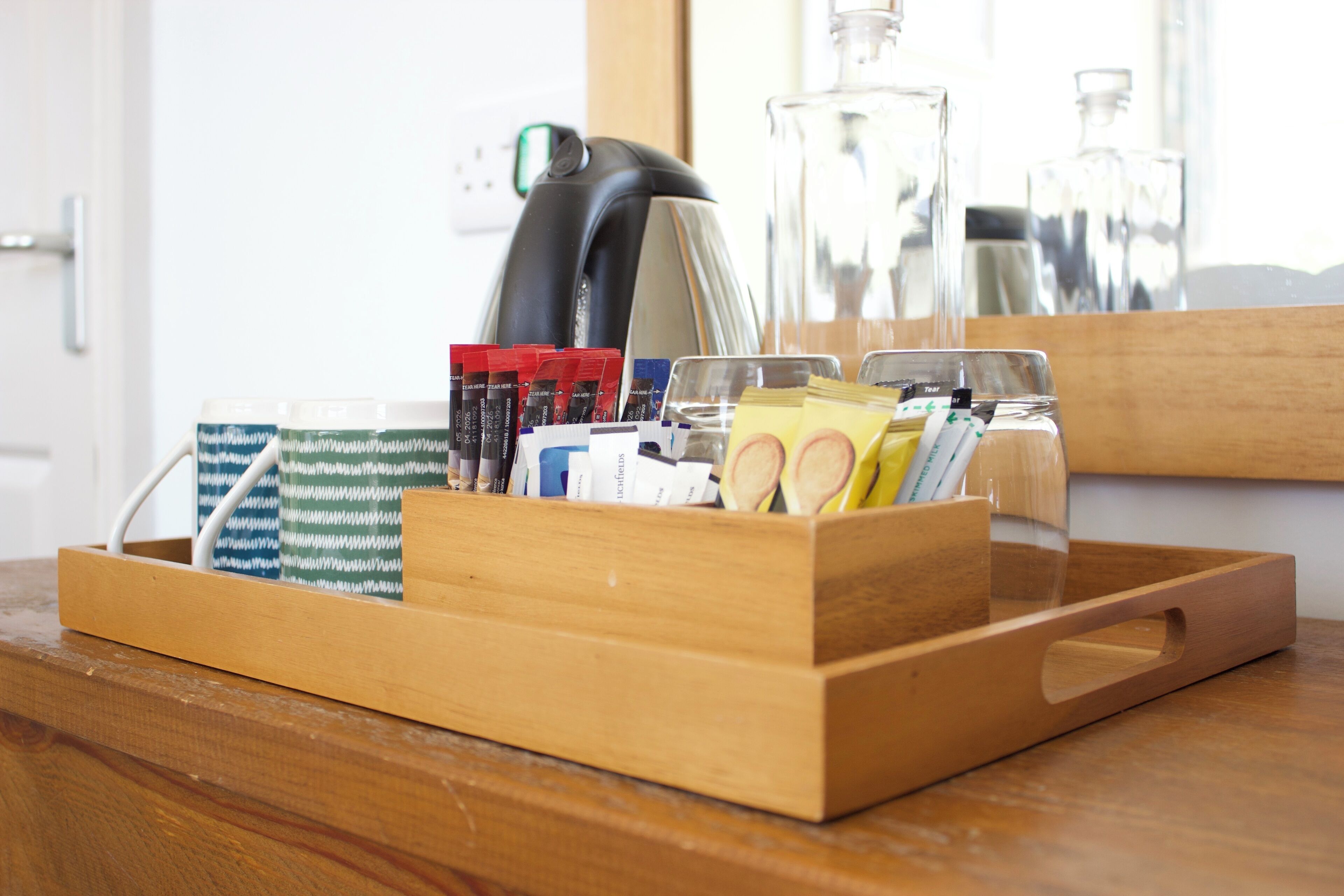 Una bandeja de madera con varios objetos, incluyendo una tetera, botellas de vidrio y paquetes, sobre una mesa de madera.
