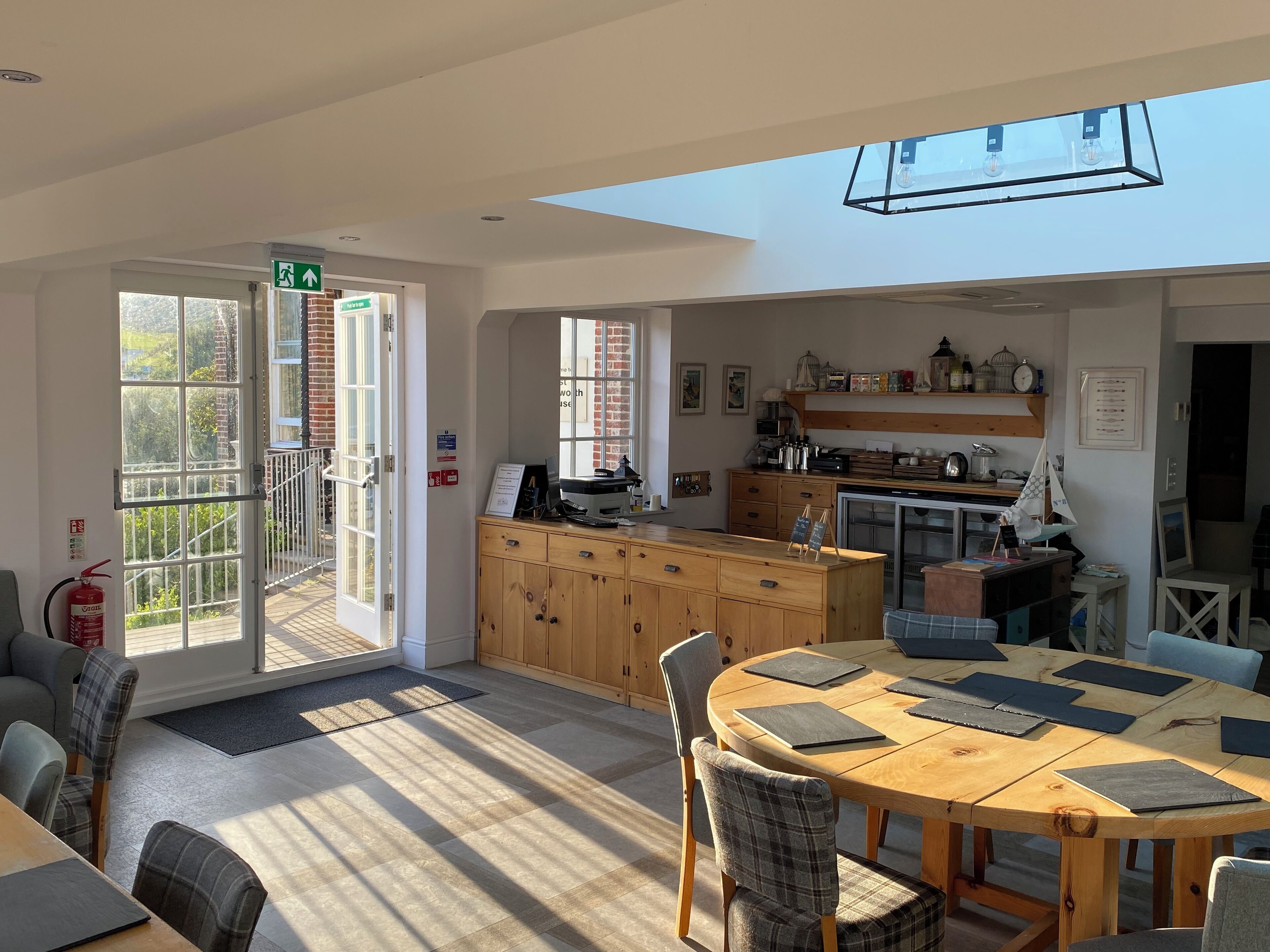 A bright, open-plan living area with a wooden dining table, chairs, and a kitchen area with a wooden cabinet and various kitchen items.