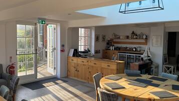 A bright, open-plan living area with a wooden dining table, chairs, and a kitchen area with a wooden cabinet and various kitchen items.