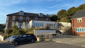 A two-story house with a garage, a small outdoor seating area, and a car parked in front. - Durdle Door Hotel (Wareham)
