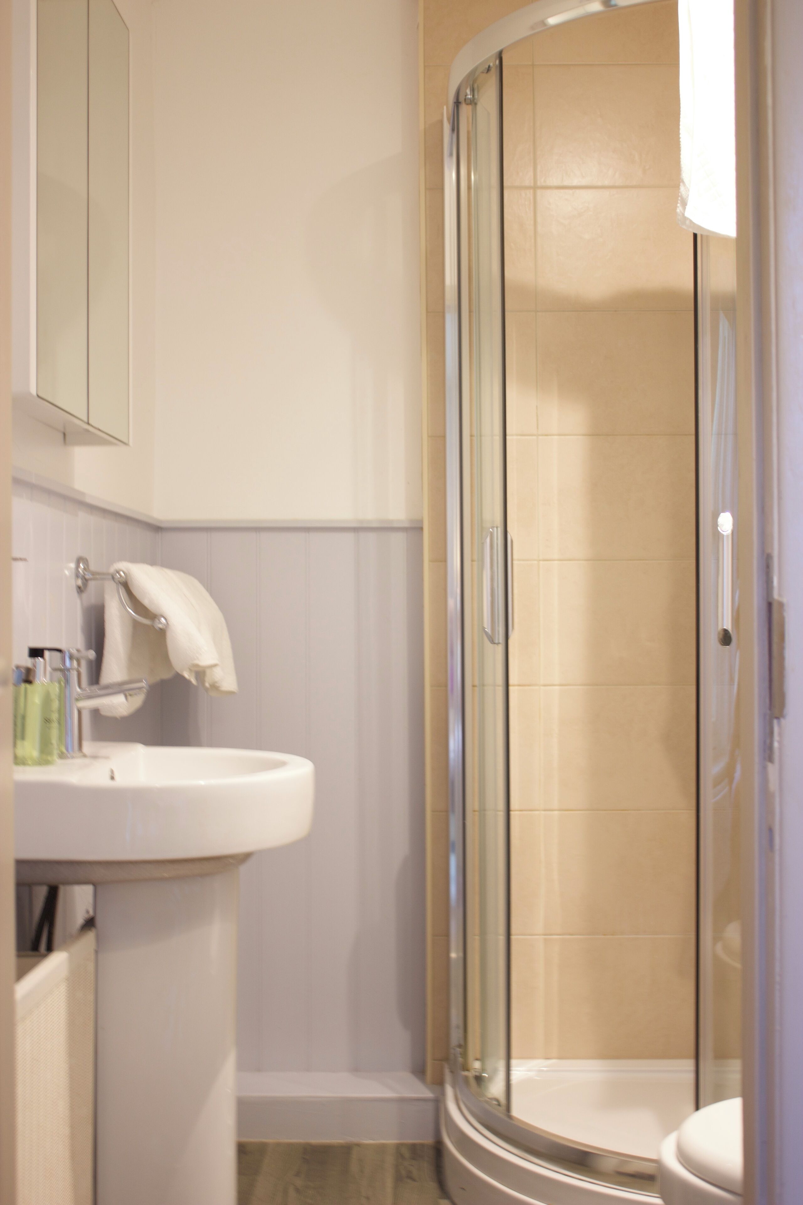 A bathroom with a glass-enclosed shower, a sink with a mirror, and a towel hanging on the wall.