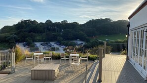 A wooden deck with outdoor seating and a view of a parking lot and greenery. - Durdle Door Hotel (Wareham)