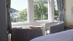 A hotel room with wicker furniture, a bed, a small table, and a view of a parking lot and trees. - Durdle Door Hotel (Wareham)