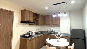 A modern kitchen with wooden cabinets, a black refrigerator, a dining table with chairs, and a ceiling light fixture.