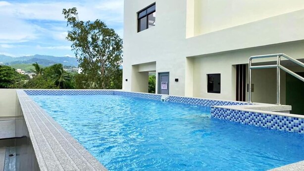 A swimming pool with a tiled edge, a metal handrail, and a view of a building with a door and window.