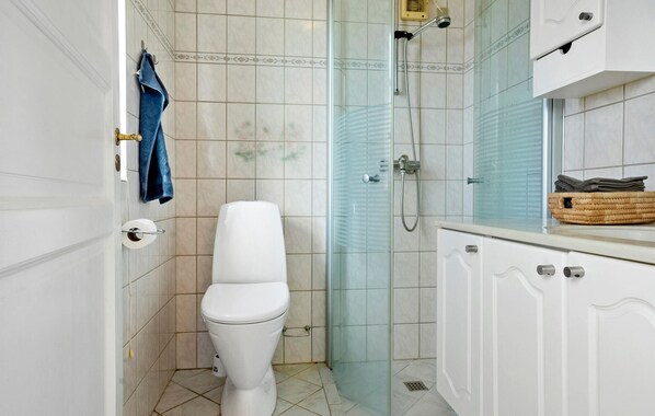 A bathroom with a toilet, a glass shower enclosure, and a cabinet with towels.