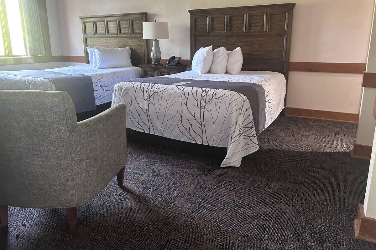 A hotel room with two beds, a chair, a nightstand with a lamp, and a telephone.