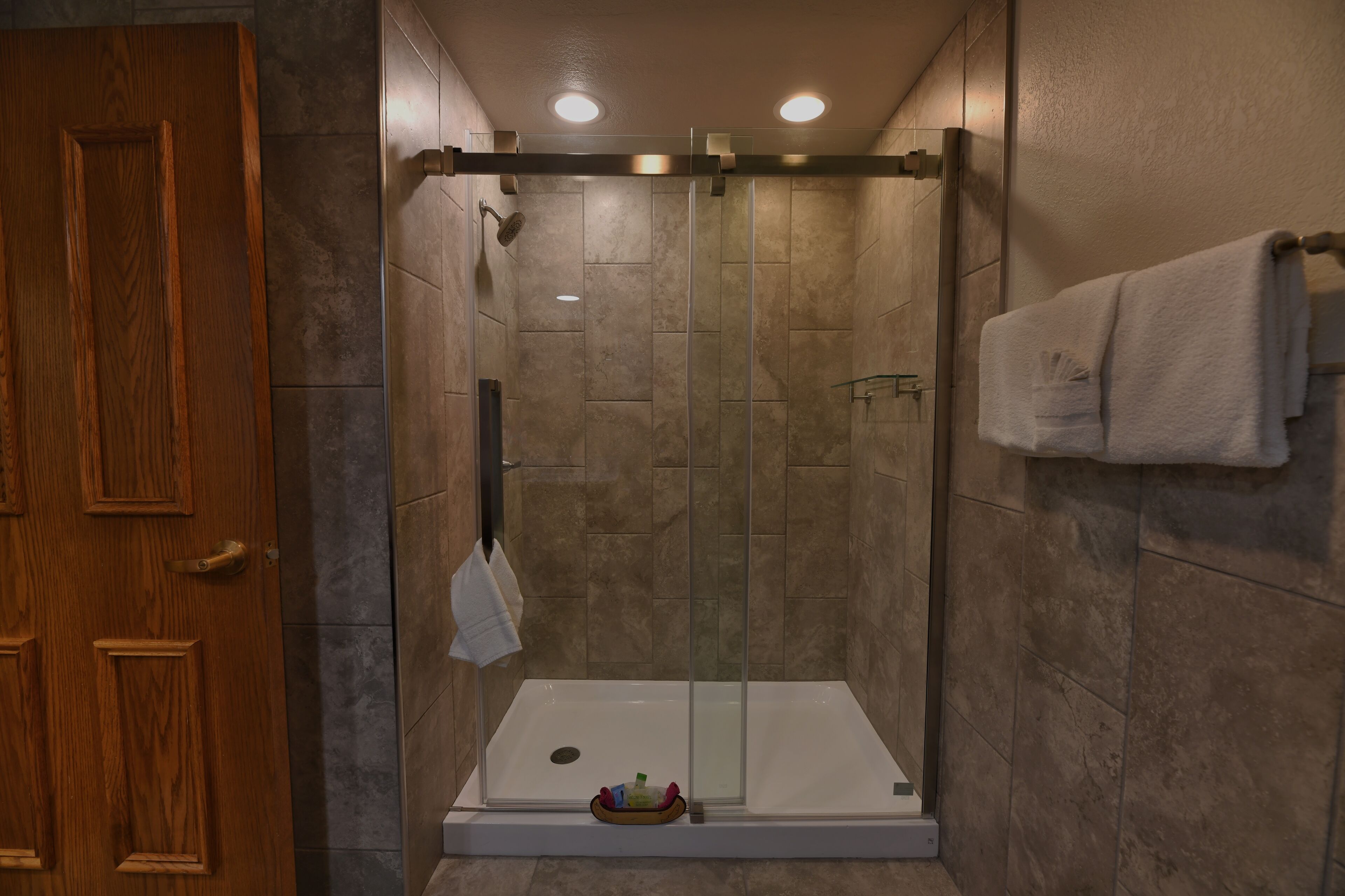 A walk-in shower with a glass door, a wooden door to the left, and a towel rack with a towel on the right.