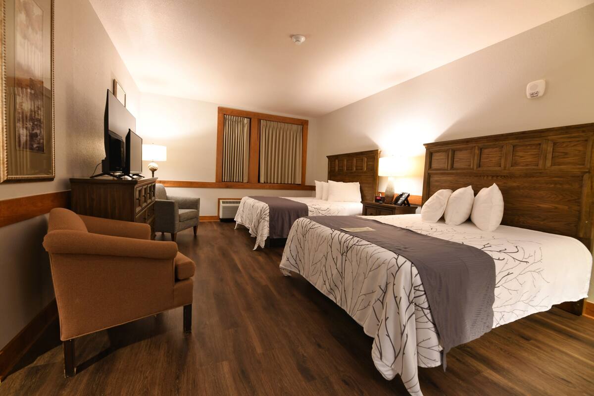 A hotel room with two beds, a TV, a desk, and a chair.