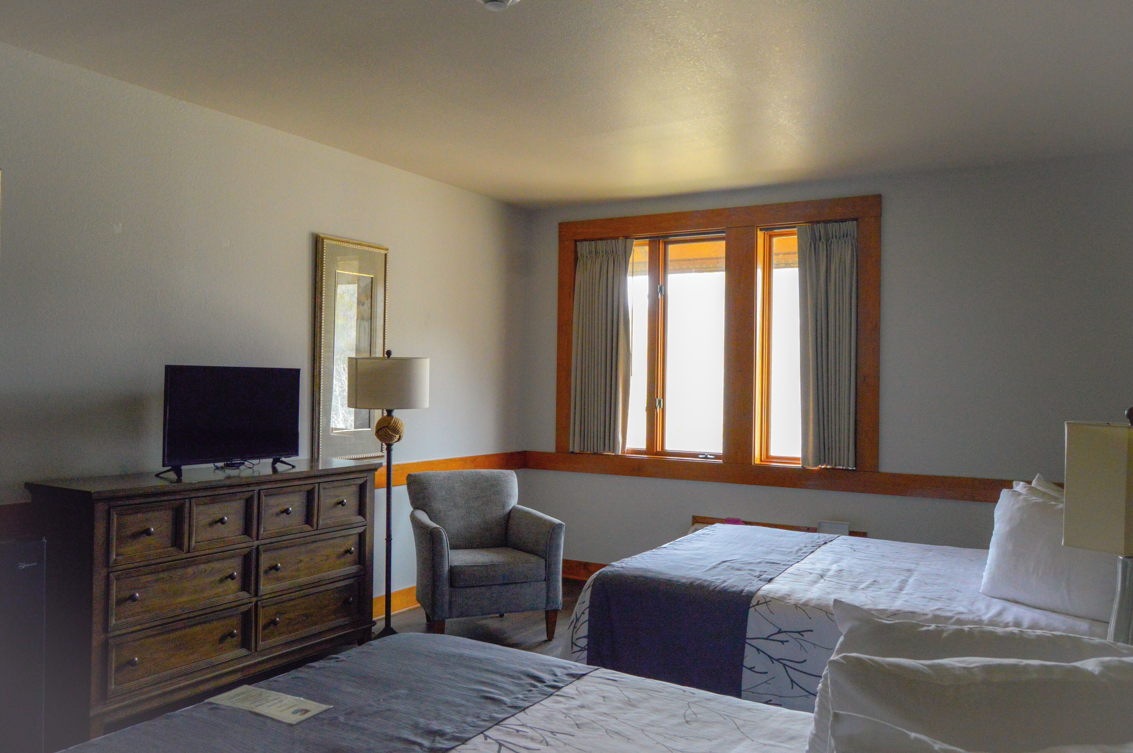 A hotel room with two beds, a dresser, a chair, a television, and a window with curtains.